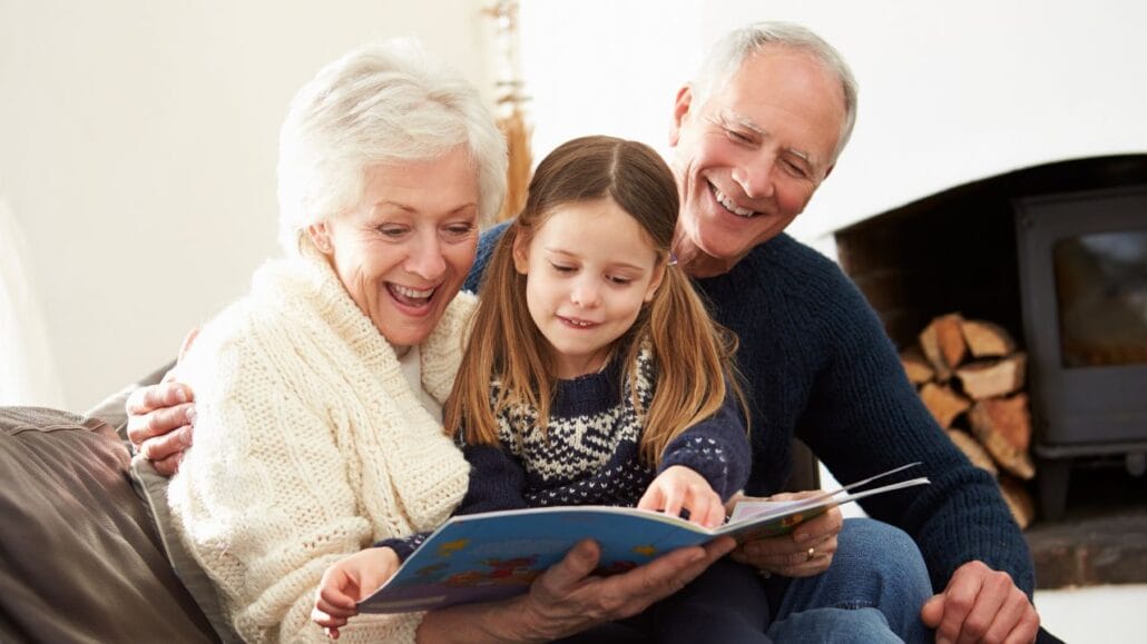 avós sentados no sofá e neta no meio com livro na mão