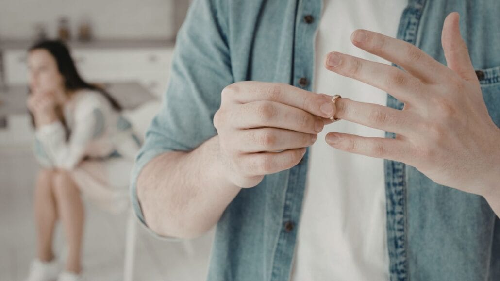 homem em primeiro plano tirando a aliança e mulher atrás após separação de fato