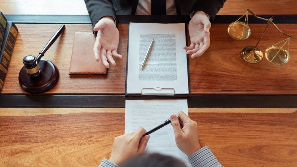 imagem de cima de advogados com papeis na mesa, balança da justiça e martelo, discutindo pontos do divórcio litigioso