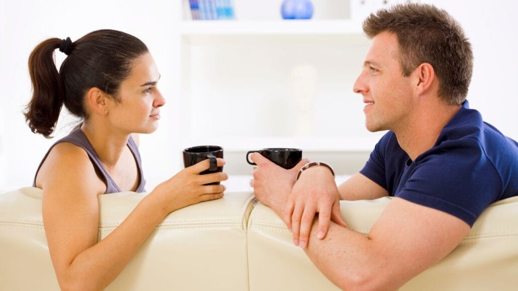 casal no sofá de frente um para o outro segurando xícaras pretas conversando sobre o regime de casamento