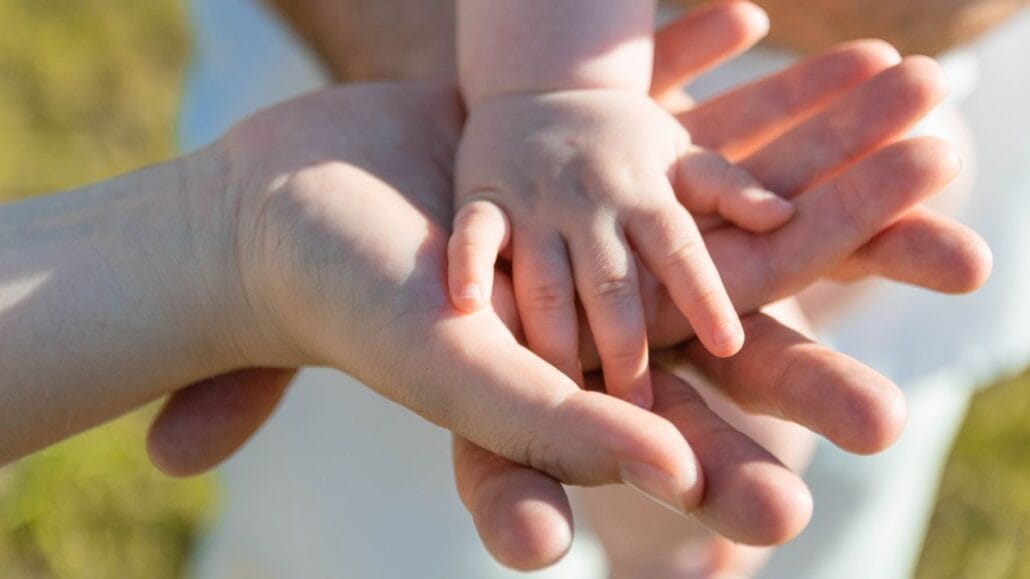 mãos de adultos sob mão de criança representando a necessidade de cuidado com a família durante o divórcio