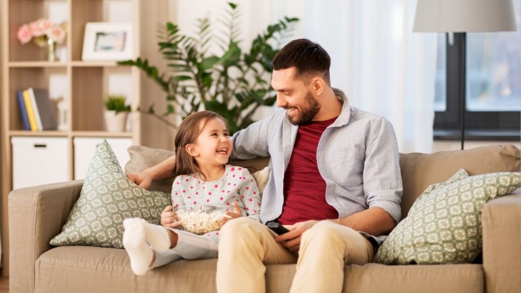 pai e filha sentados no sofá sorrindo um para o outro
